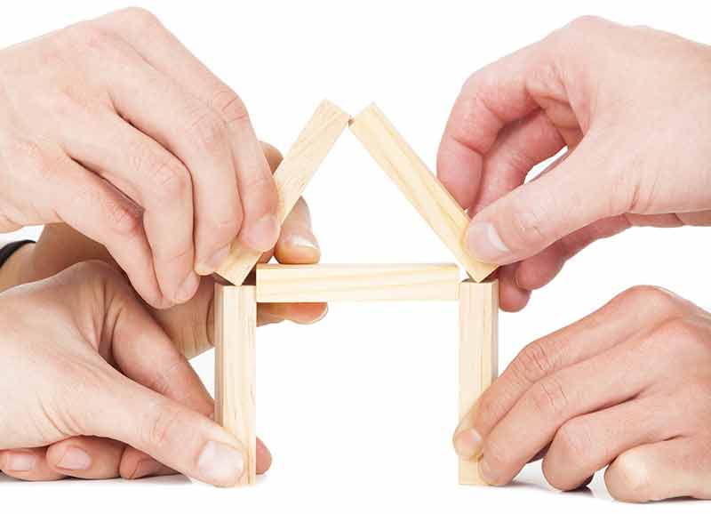 Hands building a house out of blocks.